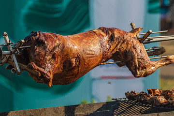 The carcass of a young sheep roasting on a spit over a low fire of burning coals. Roasted lamb on a...