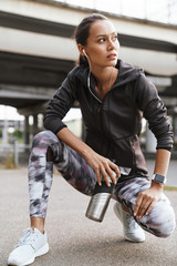 Image of young athletic woman drinking water while squatting