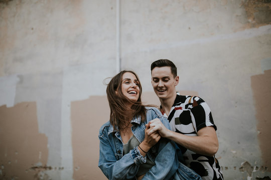 Young urban couple fist bumping each other in front of adobe wall