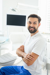 portrait of smiling doctor sitting with folded arms in modern dental clinic