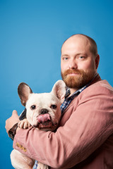 Serious man with french bulldog in arms on empty blue background