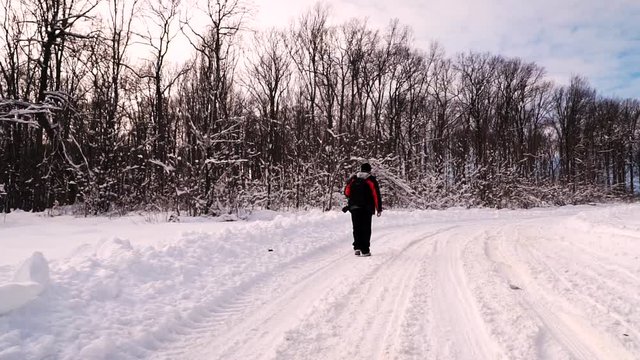 A young man walks along a path in the middle of a thick snowy forest, looking around and surprised by nature