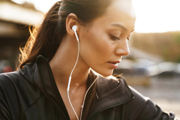 Image closeup of young focused woman using earphones while working out