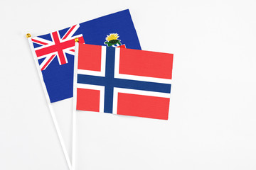 Fototapeta premium Norway and Cayman Islands stick flags on white background. High quality fabric, miniature national flag. Peaceful global concept.White floor for copy space.