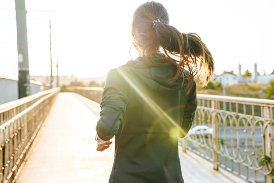 Image from back of young woman using earphones while running