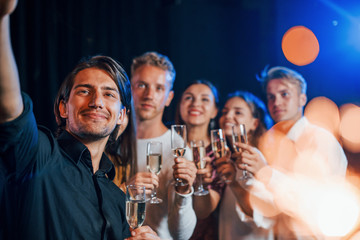 Group of cheerful friends celebrating new year indoors with drinks in hands