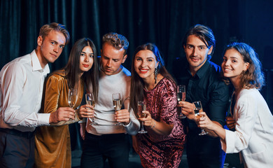 Group of cheerful friends celebrating new year indoors with drinks in hands