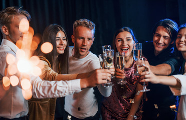 Group of cheerful friends celebrating new year indoors with drinks in hands