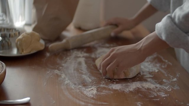 Close up of female unrecognizable hands taking wooden rolling pin and starting roll out dough for pizza