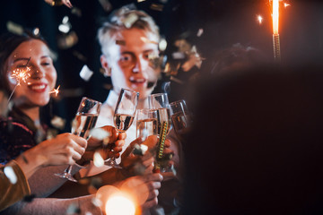 Group of cheerful friends celebrating new year indoors with drinks in hands