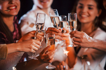 Knocking glasses. Group of cheerful friends celebrating new year indoors with drinks in hands