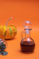 Glass jar of organic pumpkin seed oil on orange background