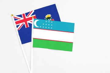 Uzbekistan and Cayman Islands stick flags on white background. High quality fabric, miniature national flag. Peaceful global concept.White floor for copy space.