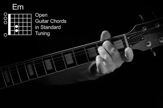 Open Guitar Chords in Standard Tuning guitar tutorial series. Closeup of hand playing Em chord on guitar, on black background. Black and white photo.