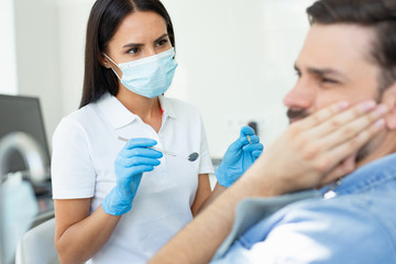 upset client touching face while having toothache near dentist in the hospital