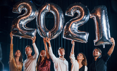 Obraz premium Cheerful group of people with drinks and balloons in hands celebrating new 2021 year