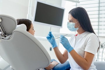 side view of dentist in mask examining teeth of small client in the hospital