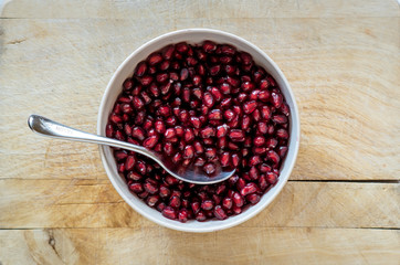 Freshly cleaned pomegranate seeds in a white bowl with a spoon