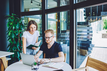 Positive male copywriter posting article on content website while female friend standing near with...