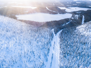 Aerial top view of snow winter mountain landscape with forests, frozen lakes and road in Finland.
