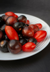 Red and black tomatoes on white plate.  Black skinned tomatoes with crimson flesh