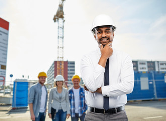 architecture, building business and people concept - smiling indian male architect in helmet over...