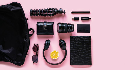 Modern black accessories, gadgets and lemon slice on pink background, top view. Flat lay composition with citrus fruit, headphones, notebook, flash drive, camera lens, sunglasses and bag