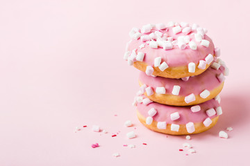 Tower of pink glazed donuts with marshmallows on pink background
