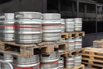 Stock of steel beer kegs on the wooden palettes. Many beer barrels at a beer factory.