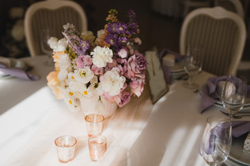 Coziness and style. Modern event design. Table setting at wedding reception. Floral compositions with beautiful flowers and greenery, candles, laying and plates on decorated table.