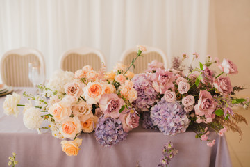 Coziness and style. Modern event design. Table setting at wedding reception. Floral compositions with beautiful flowers and greenery, candles, laying and plates on decorated table.