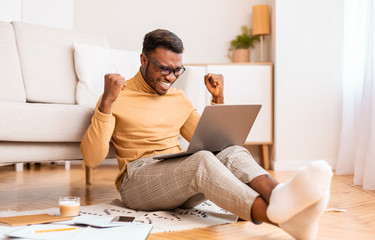 Guy Holding Laptop Shaking Fists Sitting On Floor Indoor