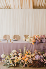 Coziness and style. Modern event design. Table setting at wedding reception. Floral compositions with beautiful flowers and greenery, candles, laying and plates on decorated table.