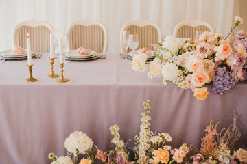 Coziness and style. Modern event design. Table setting at wedding reception. Floral compositions with beautiful flowers and greenery, candles, laying and plates on decorated table.