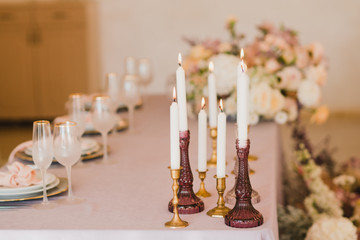 Coziness and style. Modern event design. Table setting at wedding reception. Floral compositions with beautiful flowers and greenery, candles, laying and plates on decorated table.