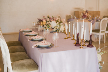 Coziness and style. Modern event design. Table setting at wedding reception. Floral compositions with beautiful flowers and greenery, candles, laying and plates on decorated table.