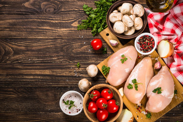 Chicken fillet with ingredients for cooking on wooden table.