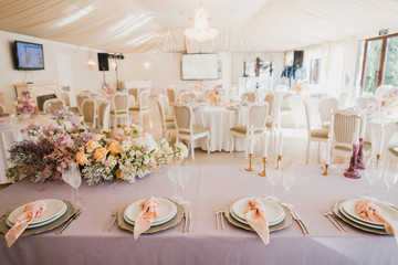 Coziness and style. Modern event design. Table setting at wedding reception. Floral compositions with beautiful flowers and greenery, candles, laying and plates on decorated table.