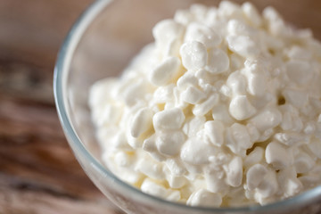 food and dairy products concept - close up of homemade cottage cheese in glass bowl on wooden table