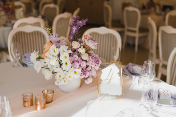 Coziness and style. Modern event design. Table setting at wedding reception. Floral compositions with beautiful flowers and greenery, candles, laying and plates on decorated table.