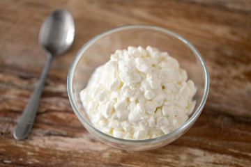 food and dairy products concept - close up of homemade cottage cheese in glass bowl on wooden table