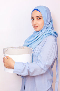 Muslim woman giving or receiving a gift on an Islamic holiday. Cute and attractive middle-eastern female in hijab holding a big present box in hands