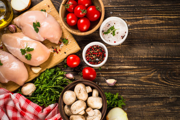 Chicken fillet with ingredients for cooking on wooden table.