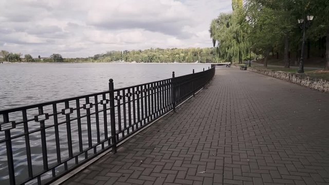 Camera movement in front of an empty lake promenade in a city park. Overcast autumn day.