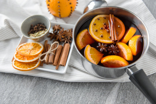 christmas and seasonal drinks concept - pot with hot mulled wine, orange slices, aromatic spices and ladle on grey background
