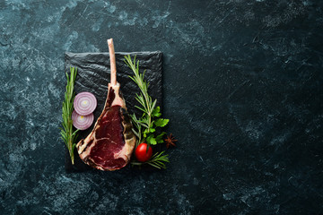 Raw dry steak on bone. Tomahawk steak on a black stone background. Top view. Free space for your...