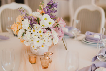 Coziness and style. Modern event design. Table setting at wedding reception. Floral compositions with beautiful flowers and greenery, candles, laying and plates on decorated table.