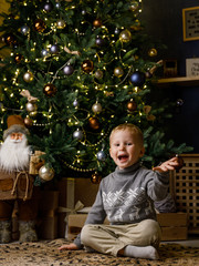 А little cute boy writes a letter to Santa Claus, dresses up a Christmas tree and dreams of a miracle on the background of the Christmas interior.