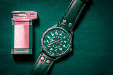 Metal lighter and men's watch on a blue-green background.