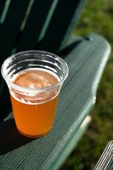 Pint of beer in a plastic cup, on the armrest of a patio chair
